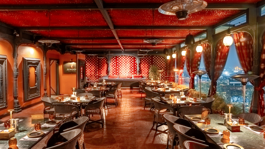 A large restaurant hall with red ceiling, long rows of dining tables and warm hanging lights at Infiniti Hotel, Indore.