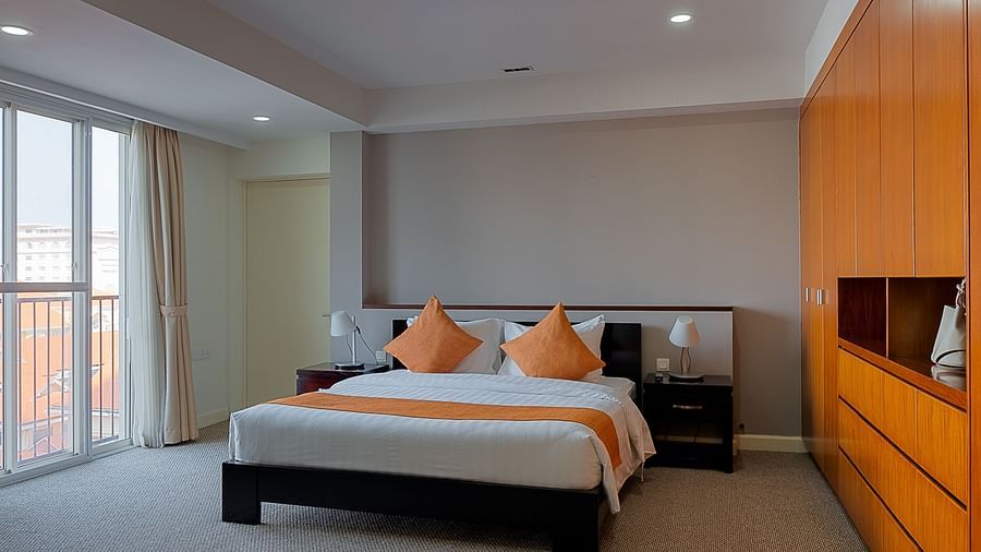 A bedroom with a bed, bedside tables, and an orange accent wall | Penthouse | Central Mansions, Phnom Penh