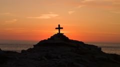A cross on a hill with the subset and the sea in the background