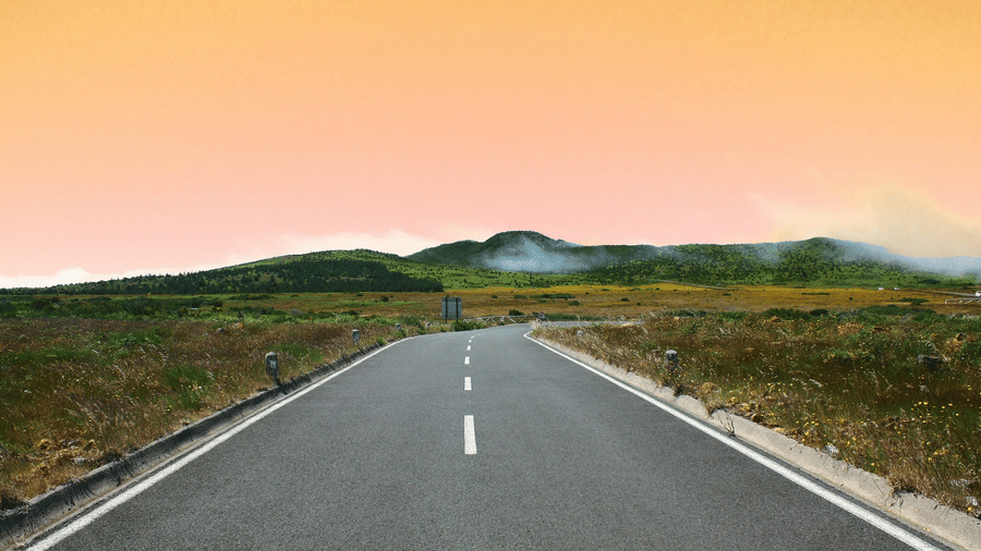 An overview of a road with vegetation on either side and an orange hued sky in view.
