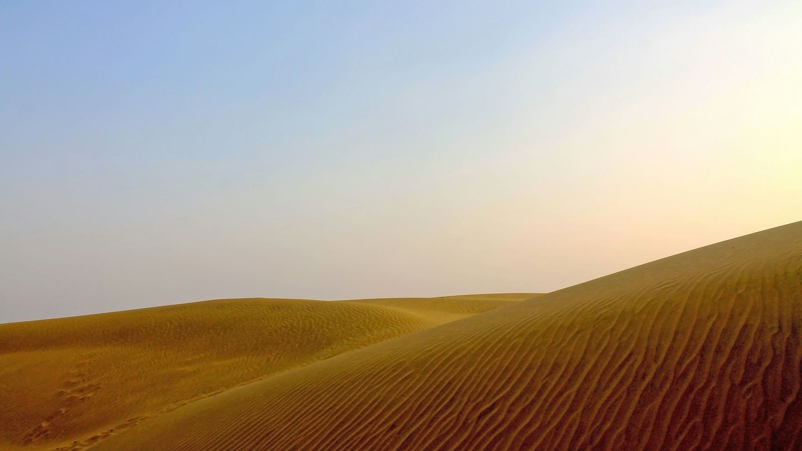 An overview of sand dunes with the sun setting in the background