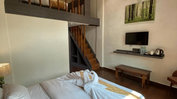 Interior shot of a duplex-style room showing the ground floor beds and the wooden stairs leading to a mezzanine level - DAN Resorts & Weddings, Palghar