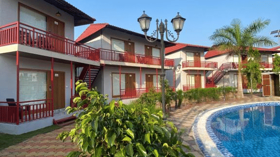 View of the curved outdoor swimming pool adjacent to 2-storey resort villas with landscaped greenery - DAN Resorts & Weddings, Palghar