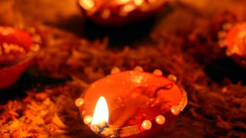  A vertical, close-up shot of several traditional clay lamps, with bright flames, placed in a line on the ground. 