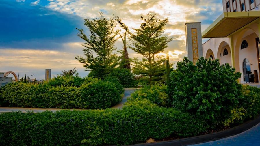 A garden foreground with hotel facade and a golden hue filed sky in the background - Serene Sarovar Premiere Hargeisa