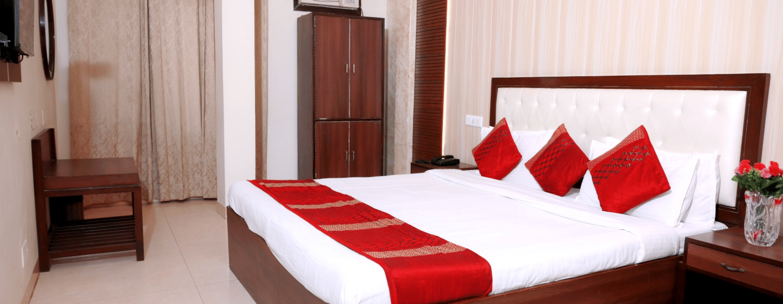 A stylish hotel room with a king-size bed, red and white linens, wooden furnishings, and elegant lighting - Hotel Diamond Inn, Chandigarh