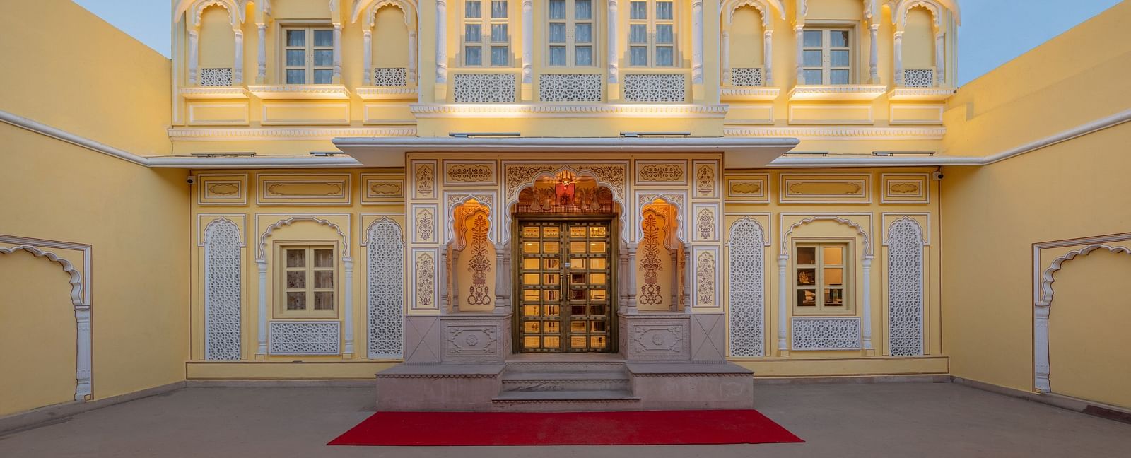 full view of the courtyard in front of the entrance door with a red carpet in front of -t - Brij Castle, Jaipur