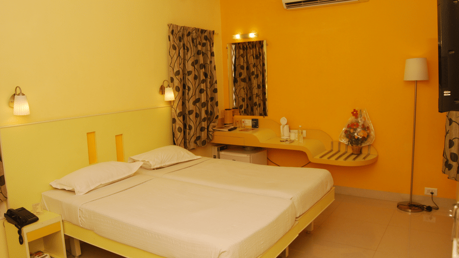 Hotel room interior featuring double bed made with crisp white linens against a bright orange accent wall - Hotel Pandian