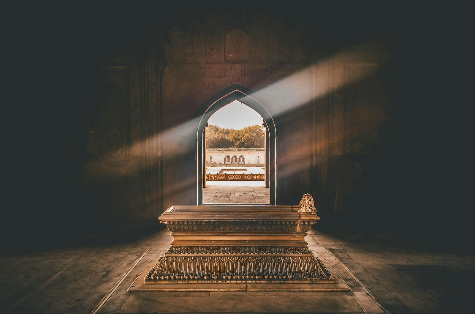 Light streams through an arched doorway onto a patterned carpet in a dark room.