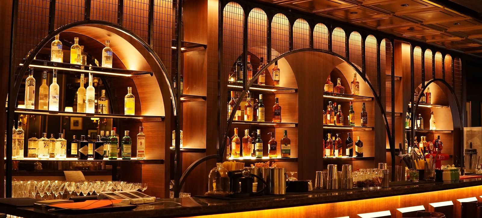 A dimly lit bar with a wooden counter, shelves filled with bottles of liquor, and warm lighting.