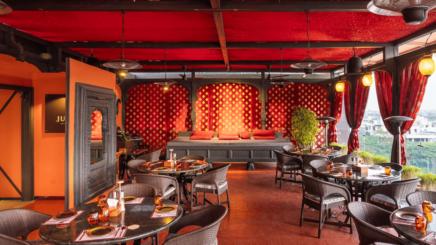 A restaurant interior with red ceiling, patterned walls, and dining tables with chairs at Infiniti Hotel, Indore.