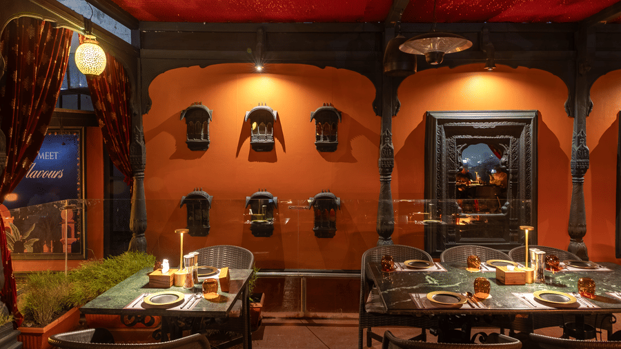 A restaurant interior with warm orange walls, decorative shelves and dining tables with chairs at Infiniti Hotel, Indore.