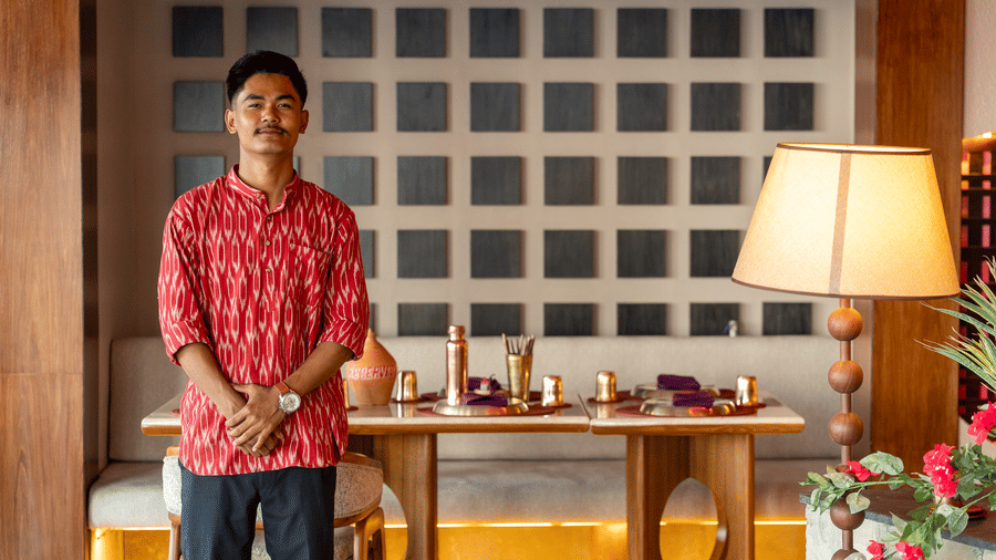 Staff member standing inside Jamun restaurant beside a table setup and decorative lighting - Symphony Resorts