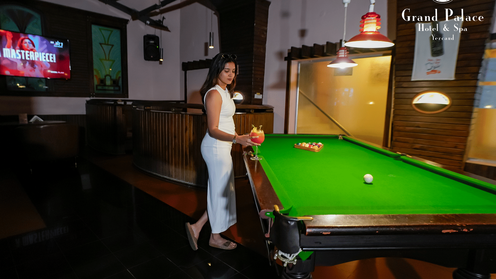 Person playing billiards at Cloud-9 Bar, Grand Palace, Yercaud with bar counter, seating booths, and wall-mounted television.