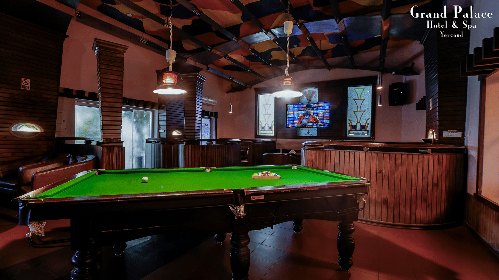 Billiards table inside Cloud-9 Bar at Grand Palace, Yercaud with television screen, hanging lights, and wooden ceiling panels.