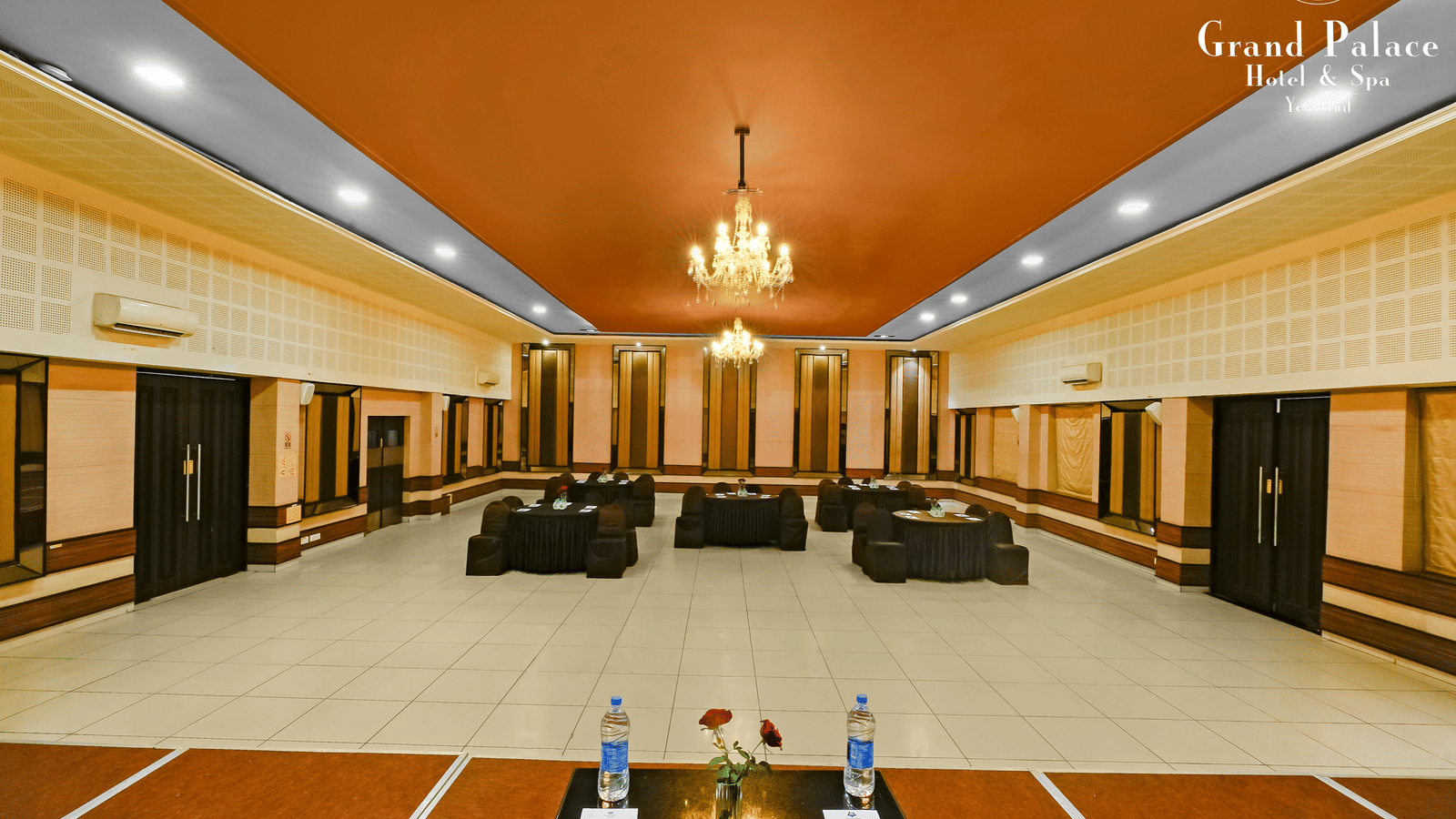 Banquet hall at Grand Palace, Yercaud with round tables, dining chairs, stage, spotlights, golden ceiling feature, and audio equipment set up for function.