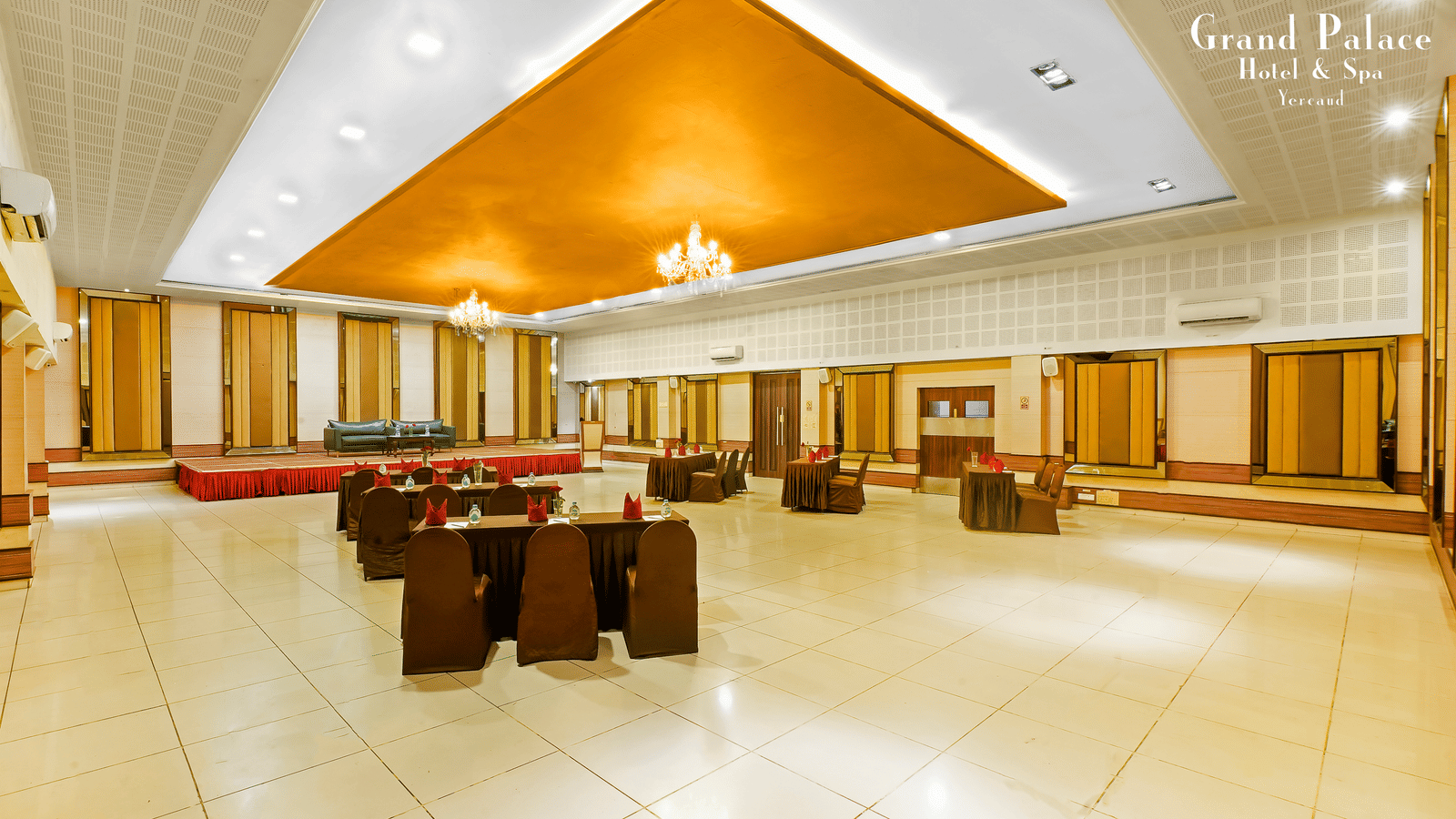 A corner view of the event space area at Grand Palace, Yercaud arranged with sofa seating, open area, chandeliers, panoramic windows, and polished flooring for gatherings.