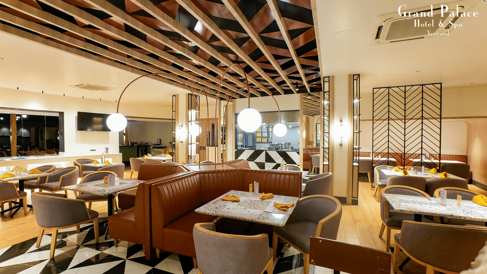 Orange Restaurant dining area at Grand Palace, Yercaud with tables, chairs, ceiling beams, and patterned flooring near the buffet section.