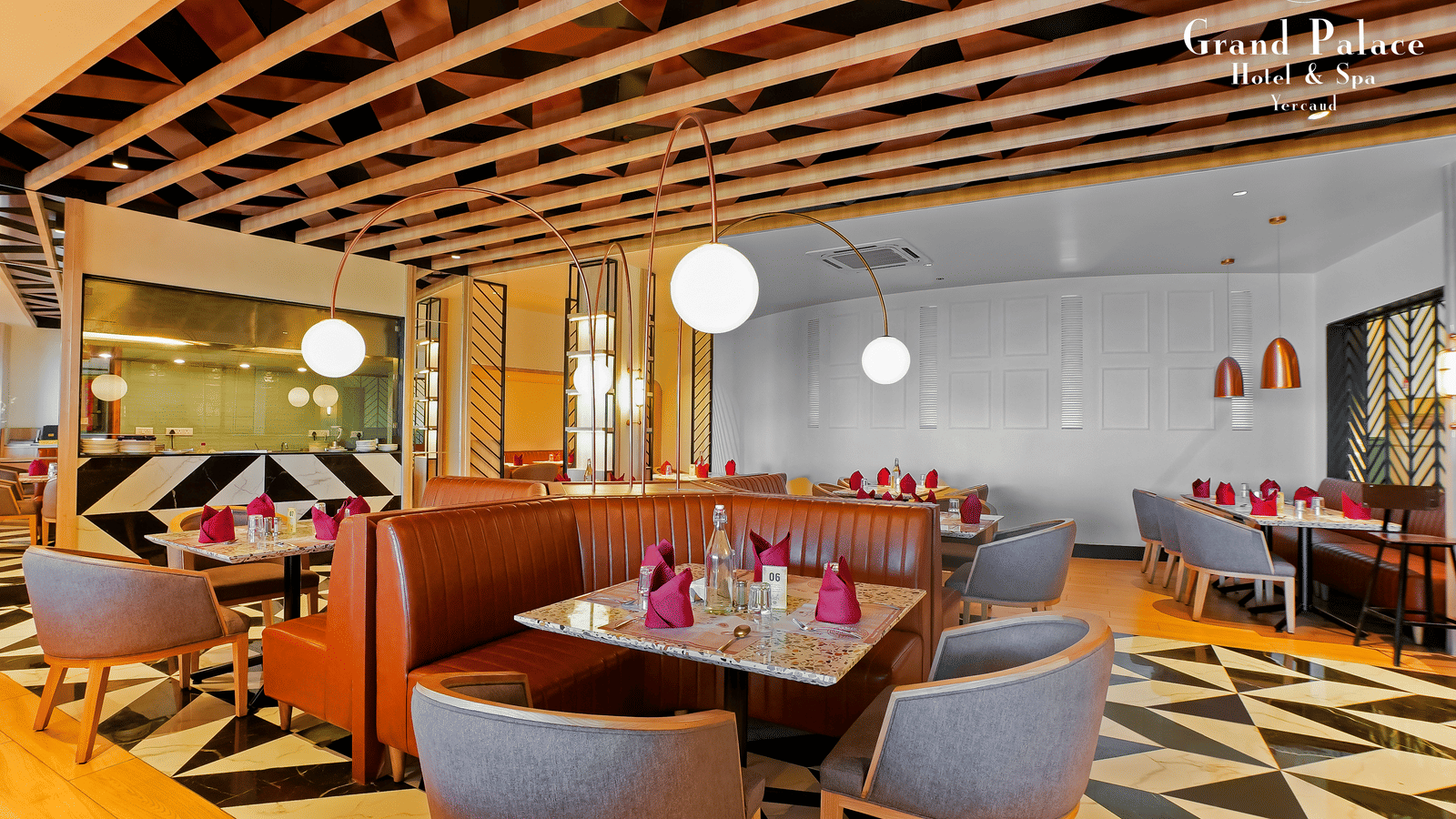Orange Restaurant interior at Grand Palace, Yercaud with dining tables, cushioned seating, ceiling beams, and wall lighting.