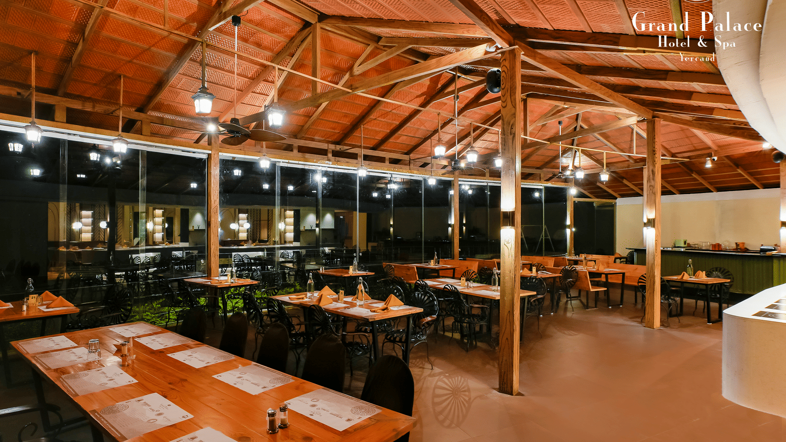 Outdoor restaurant section at Grand Palace, Yercaud showing tables, chairs, and open layout under wooden roofing.