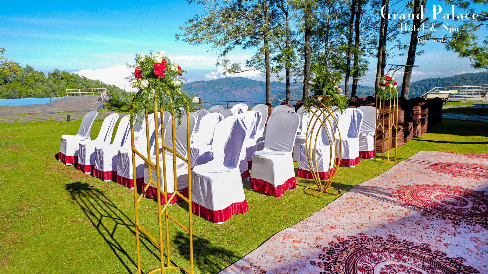 Open-air wedding seating at Grand Palace, Yercaud, showing decorated white chairs, petals, green lawn, aisle runner, trees, floral stands, and sunlight.