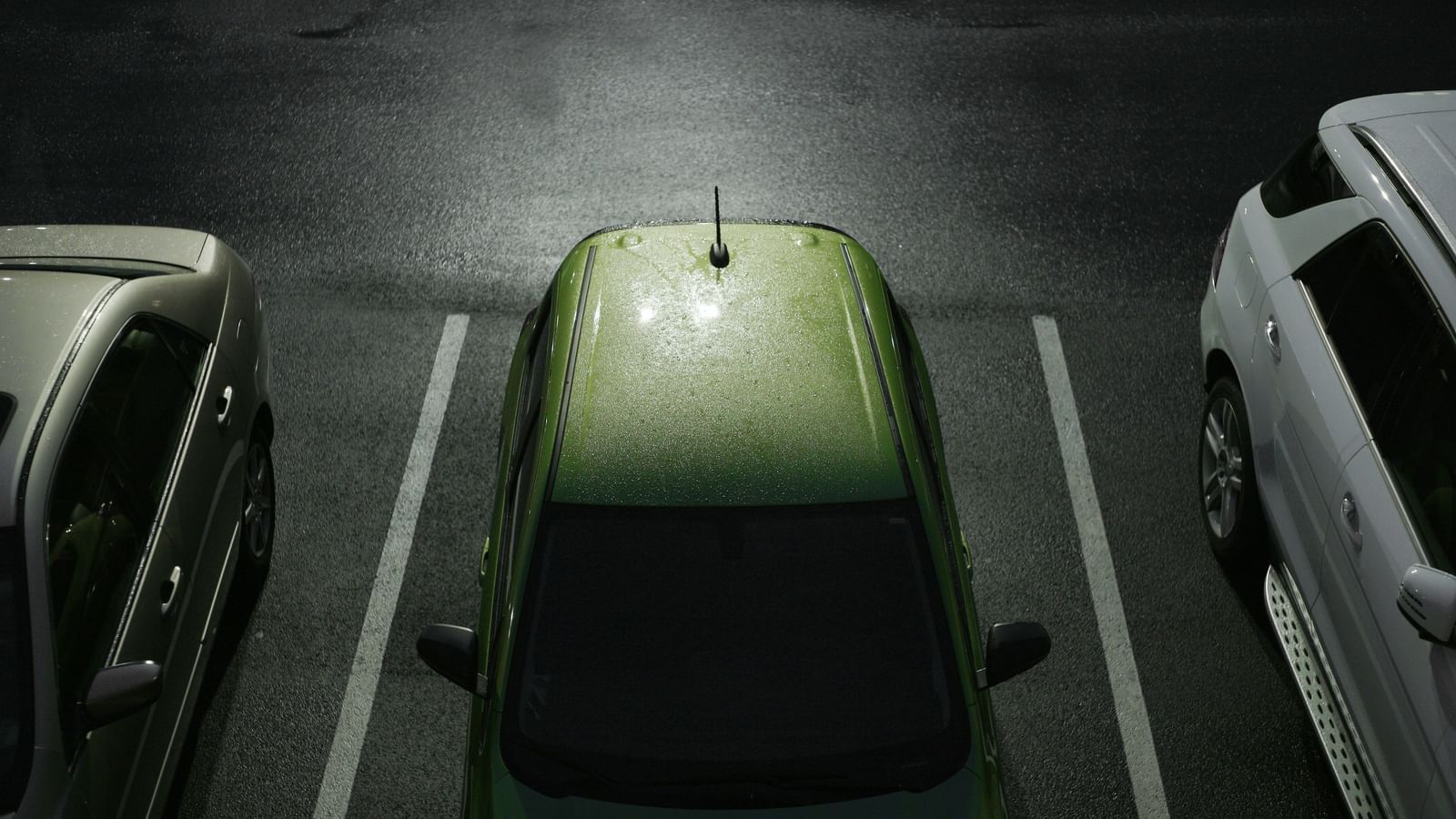 An overhead view of a light green car parked in a dimly lit parking lot.