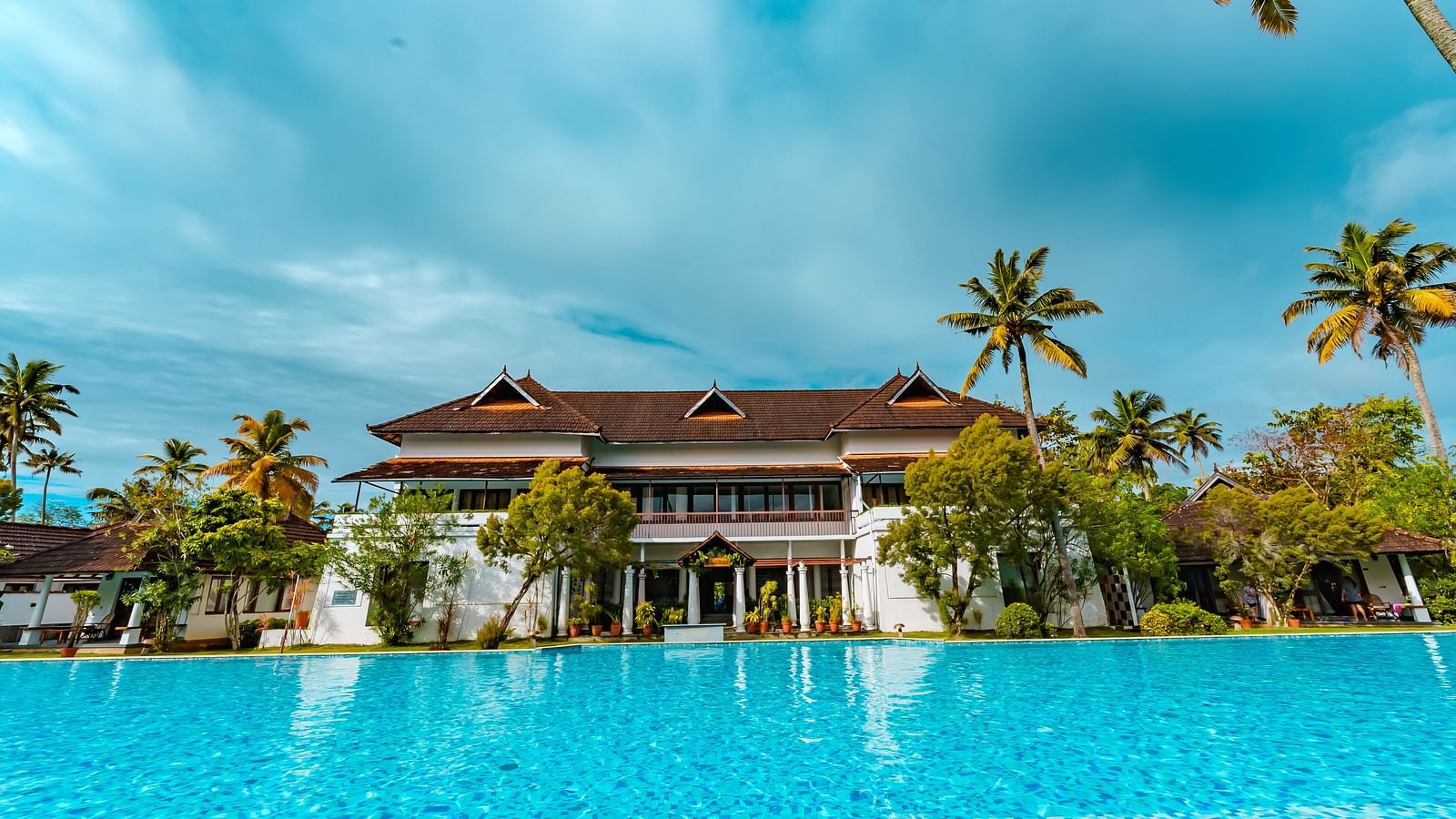 facade image of the spa from with a pool in front of it surrounded coconut trees - Rhythm Kumarakom.