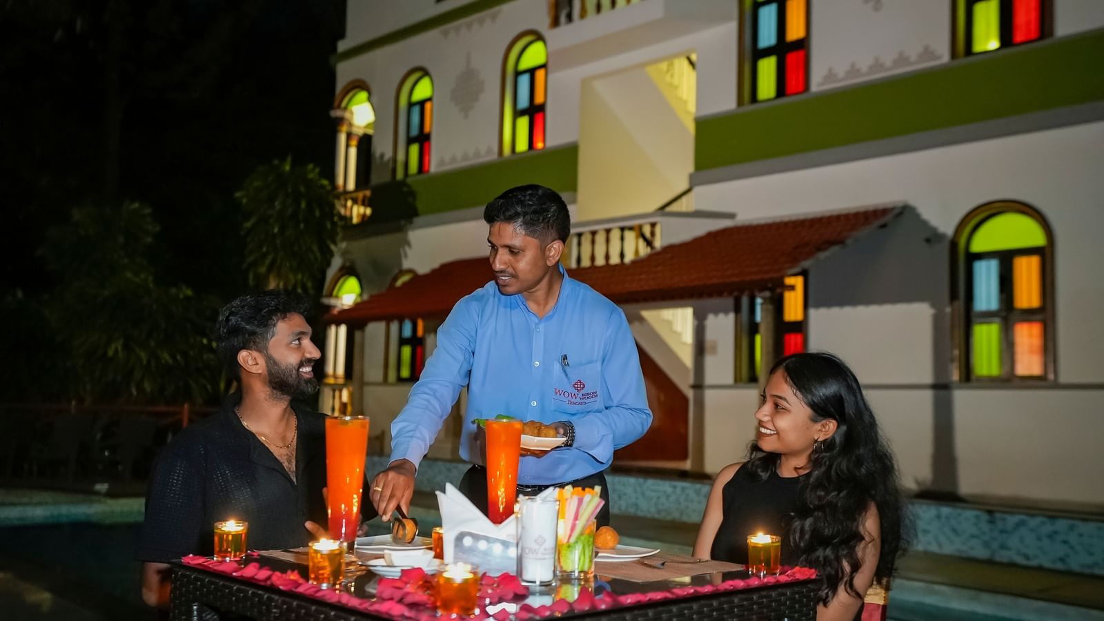 A couple having a meal outdoors with a waiter serving them.
