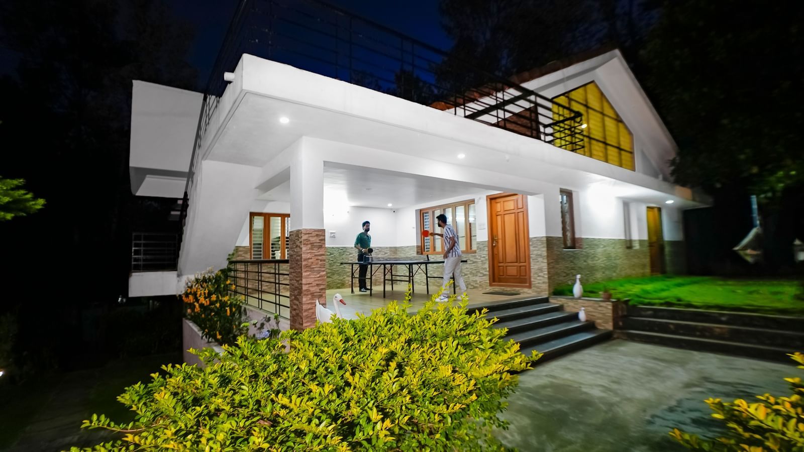 Facade view of WOW Bungalow, Yercaud, with two people playing table tennis on the porch.