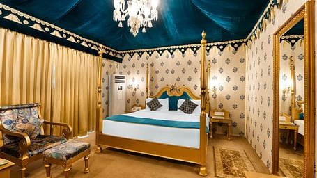 An overview of a tent with a double bed, a chair and a table seen inside it - Rajasthali Resort & Spa, Jaipur.