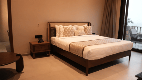 A spacious bedroom boasts a large bed with plush bedding next to glass doors opening onto a scenic balcony - Sajjan Bagh Resort and Spa, Kumbhalgarh