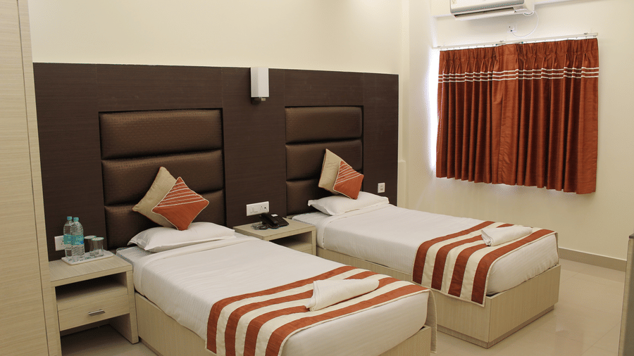 Interiors of a Deluxe Room at Hotel Shompen, offering the finest stay in Port Blair, featuring twin beds with upholstered headboards and a window with its curtain closed.