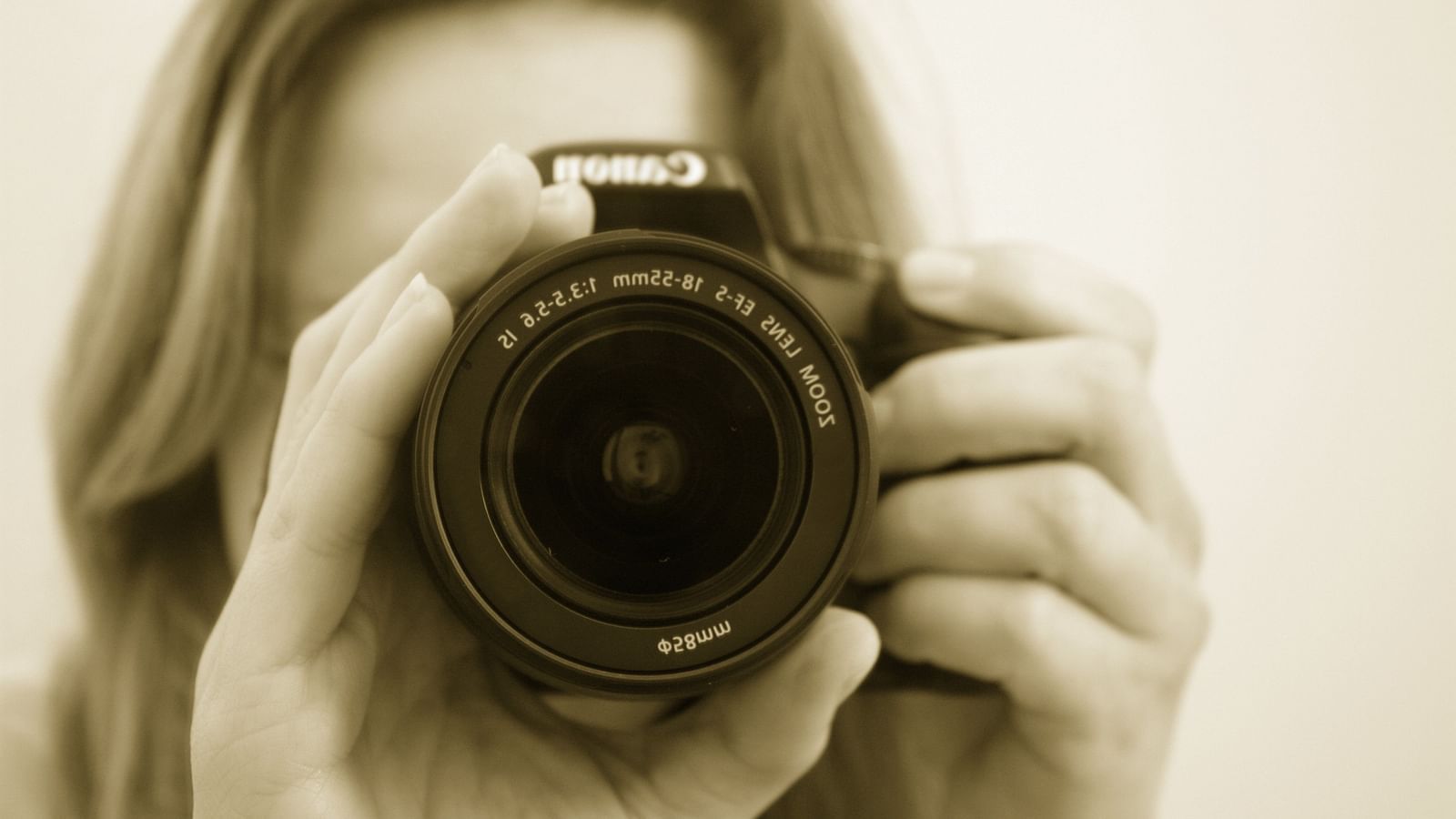 A close up shot of a woman holding a DSRL camera while adjusting the zoom.