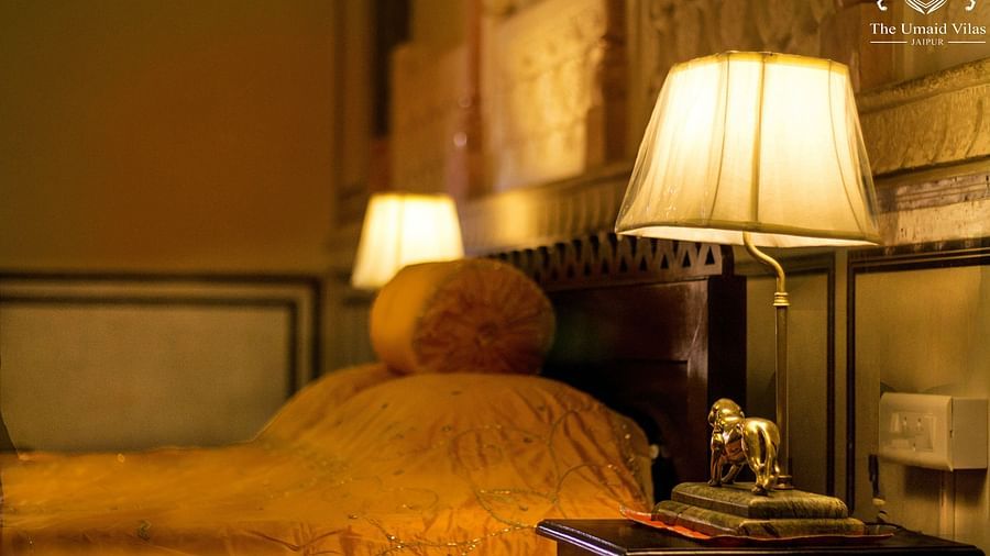 A dimly lit bedroom at Umaid Vilas Jaipur with two lamps on bedside tables, illuminating a bed with a golden throw.