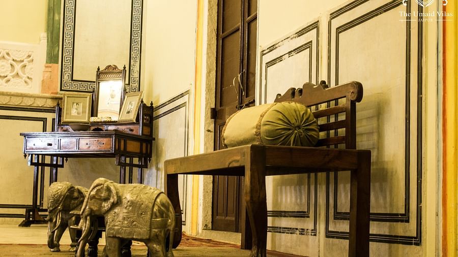 A room at Umaid Vilas Jaipur with a wooden bench, elephant sculptures, and a desk with a mirror.