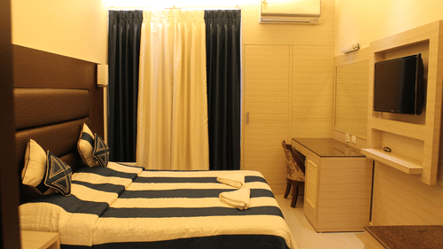 Interiors of the Deluxe Room at Hotel Shompen featuring a double bed, wall-mounted TV, and elegant blue and white curtains, ideal for travellers exploring the best Port Blair hotel deals.