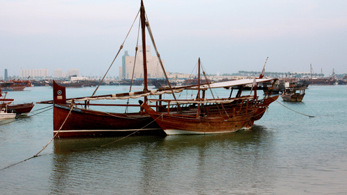 A parked Dhow boat with another small boat next to it in the water near Qatar.