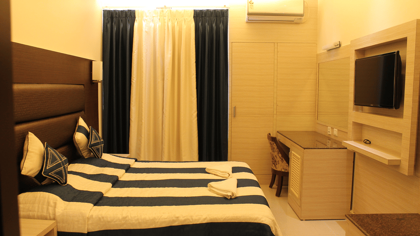 Interiors of the Deluxe Room at Hotel Shompen featuring a double bed, wall-mounted TV, and elegant blue and white curtains, ideal for travellers exploring the best Port Blair hotel deals.