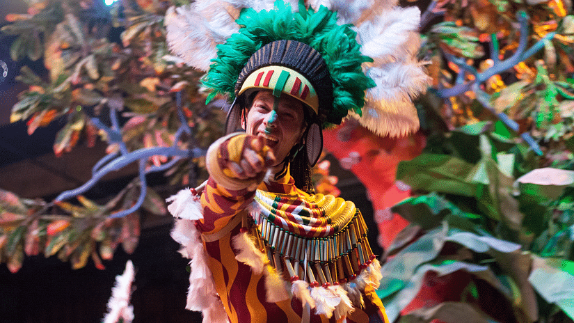 a man dress in fancy tribal clothing dressed up for a fiesta and pointing at the camera
