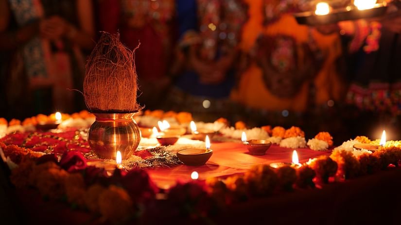 A coconut kept on the a brass bowl with diyas and balls of flowers kept next to it