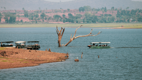 Boat safari on the Kabini River with many people inside the boat and hills in the background.
