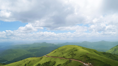 Green hill with a winding road, seen under a cloudy sky.