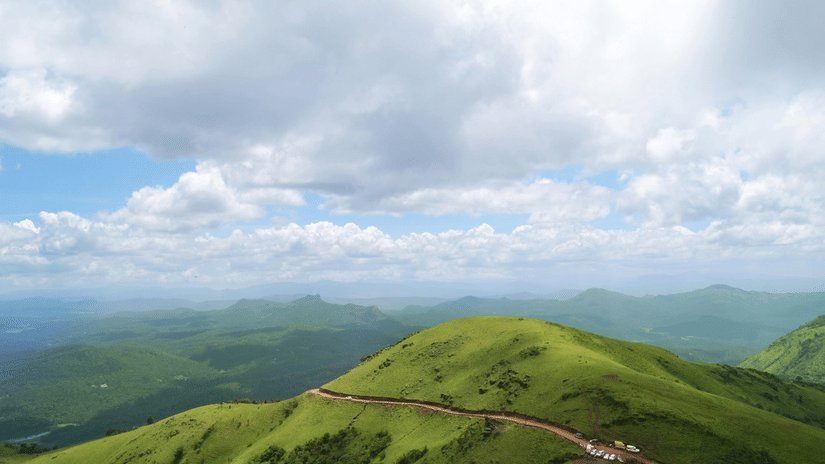 Green hill with winding road under a cloudy sky.