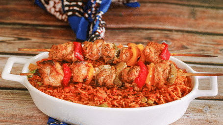 A close-up of a bowl filled with jollof rice with chicken skewers. It is one of the traditional food of Ghana.