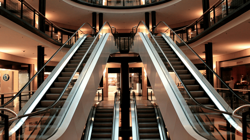 A view of the interior of a multi-level building, likely a shopping mall, showing a pair of escalators going up and another pair going down, with balconies on the upper floors and a circular open space above.