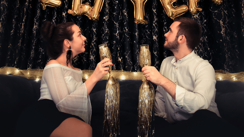 A couple holding drinks with happy new year made out of ballons on the wall