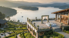 Hilltop resort terrace overlooking a wide lake at sunset, with manicured lawns and a couple standing near the edge.