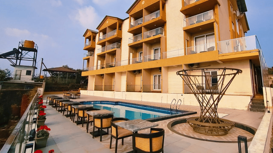 An outdoor patio with seating and a swimming pool sits beside a multi-story building at Savyasaachii Hotel.