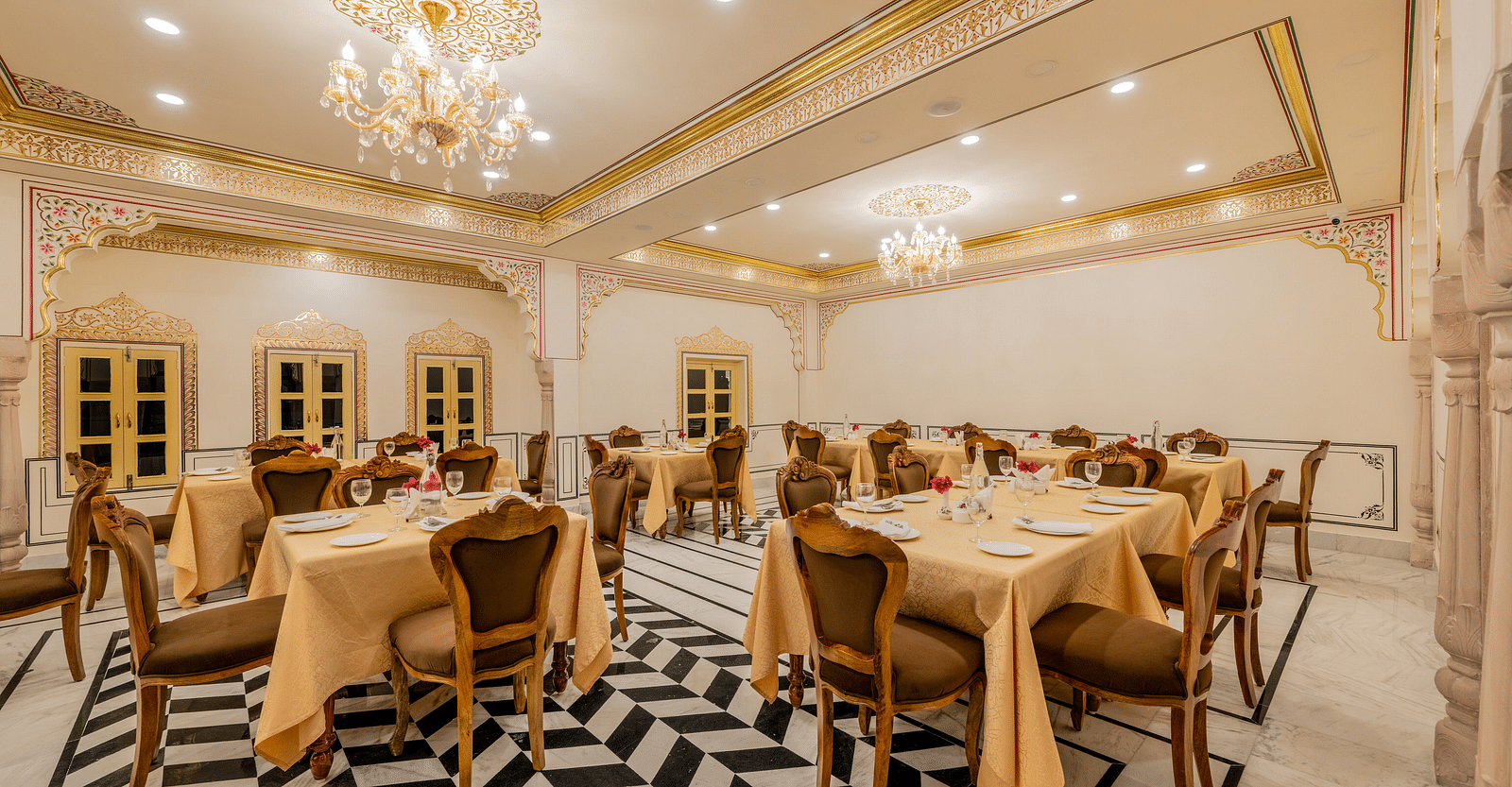 corner view image of the dining area with four windows in the far end of the restaurant and chandeliers hanging from the ceiling - Brij Castle, Jaipur