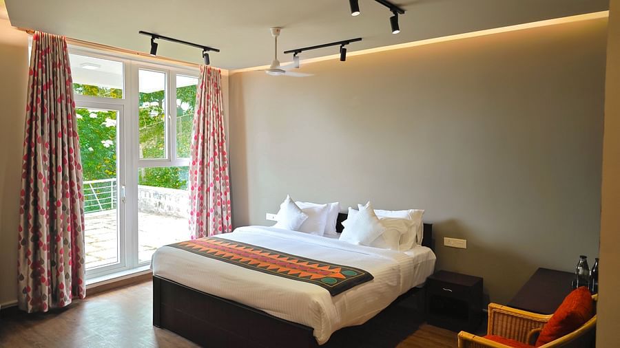 Bright bedroom with large windows, patterned curtains, a double bed, and clean, modern furnishings at Ibex Resorts, Coonoor (Tapas).